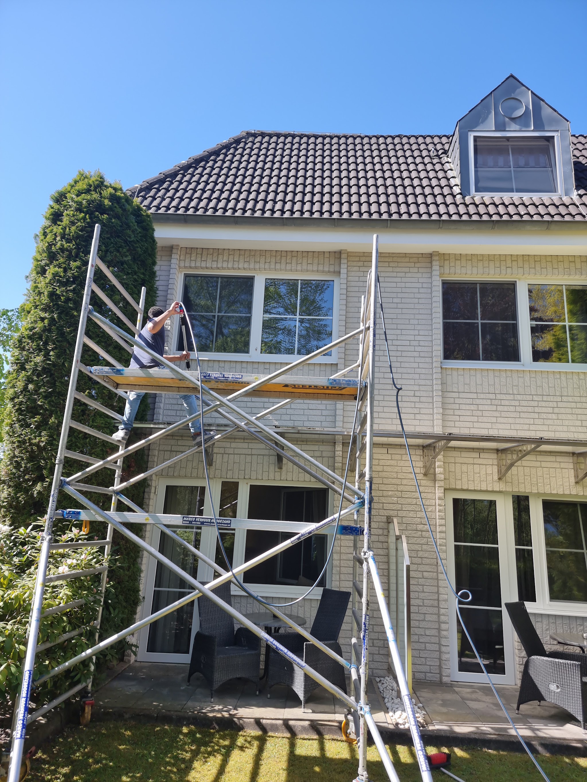 Schoonmaker op een rolsteiger wast de bovenramen van een woning